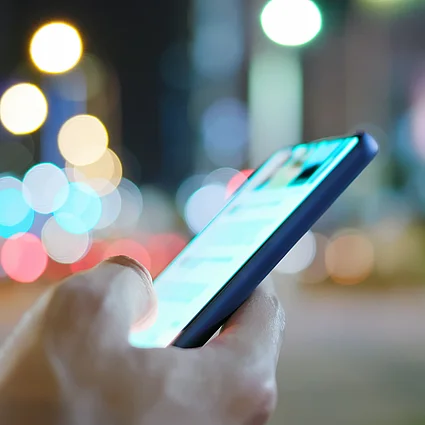 Hand hält Smartphone in nächtlicher Umgebung, Symbol für digitale Kommunikation und mobile Vernetzung.