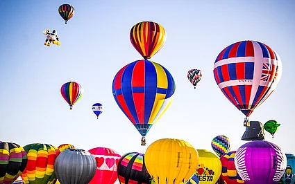 Viele bunte Heißluftballons steigen bei klarem Himmel über einem Ballonfestival auf.