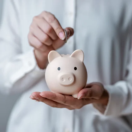Person steckt Münze in Sparschwein als Symbol für Sparen und finanzielle Vorsorge.