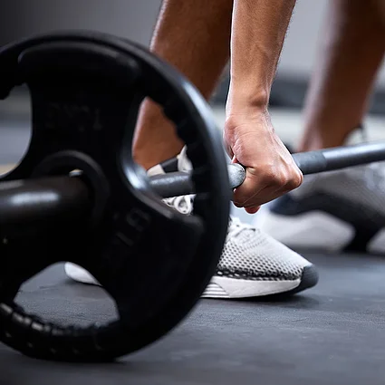 Person hebt Langhantel im Fitnessstudio als Symbol für körperliche Fitness, Disziplin und Krafttraining.